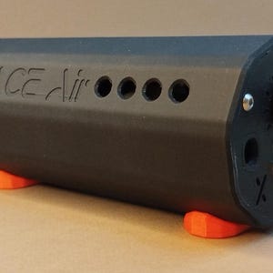 May include: A matte black hexagonal electronic device with the text SPACE AIR embossed on the side. It features four circular holes, a black control knob with a red center, a metallic input jack, and two bright orange feet for stability.