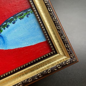 May include: Close-up of a framed painting with a vibrant color palette. The artwork features a bold red background, a light blue shape, and green accents. The frame is ornate, with gold and dark brown detailing.