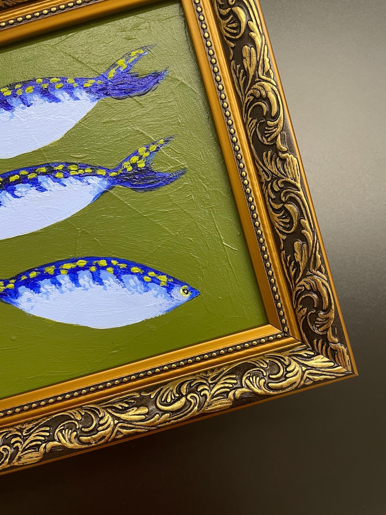 May include: An oil painting of three stylized fish with blue and yellow markings on a green background. The fish are set in a gold ornate frame. The painting has a textured surface.