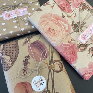 May include: Three wrapped gifts with decorative paper and twine. One is covered in white hearts on brown paper, another with pink roses, and the third with macarons and lavender. Each gift has a "Thank you" sticker.