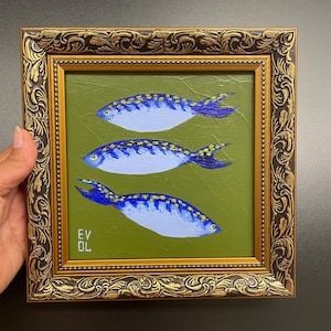 May include: A framed painting featuring three blue and yellow fish on a green background. The fish are painted with detailed scales and fins. The frame is ornate with gold and brown tones. The artist's initials, EV DL, are visible in the lower left corner.
