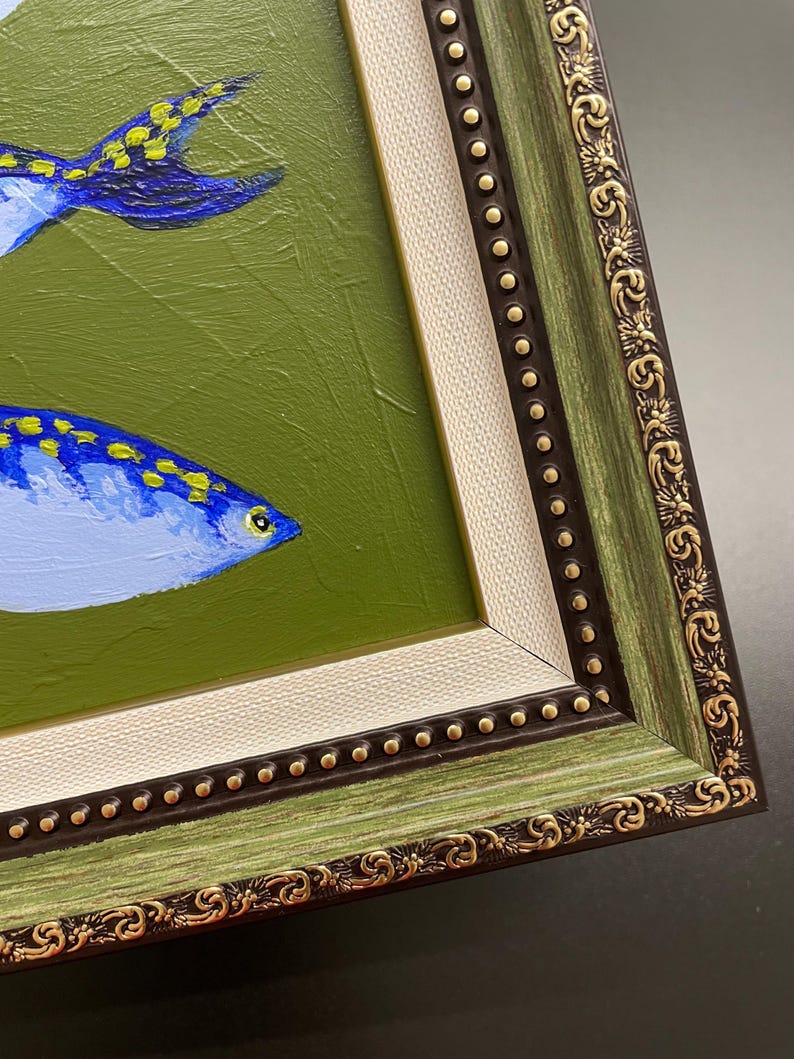 May include: An original framed painting featuring two blue fish with yellow spots against a green background. The frame is green with gold accents and a cream-colored inner border. The artwork is a close-up view.