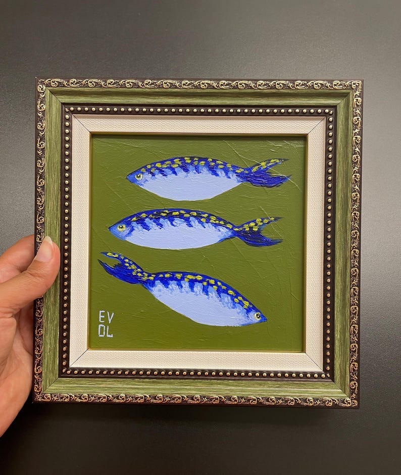 May include: An original painting of three blue fish with yellow accents on a green background. The artwork is framed in a decorative green and gold frame. The artist's initials, EV OL, are visible in the lower left corner.