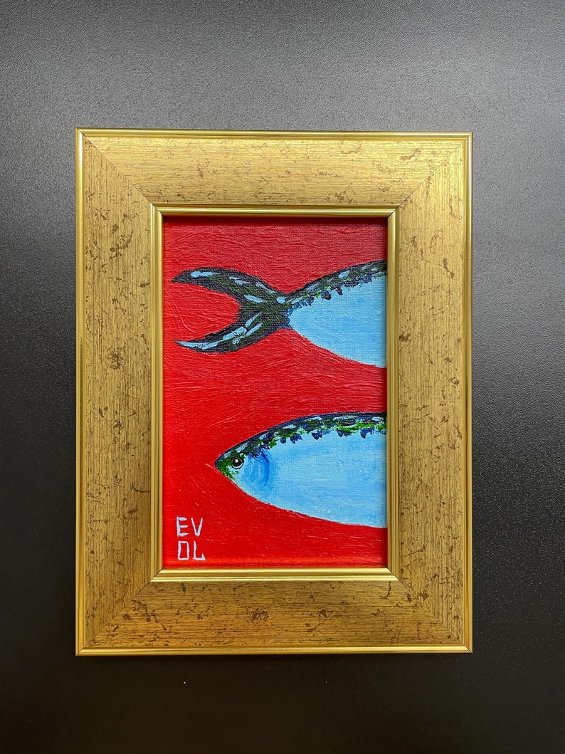 May include: A framed painting of two blue fish on a red background. The fish have detailed scales and are set against a vibrant red backdrop. The frame is gold-colored, adding a touch of elegance to the artwork. The painting is signed with the initials "EV DL".