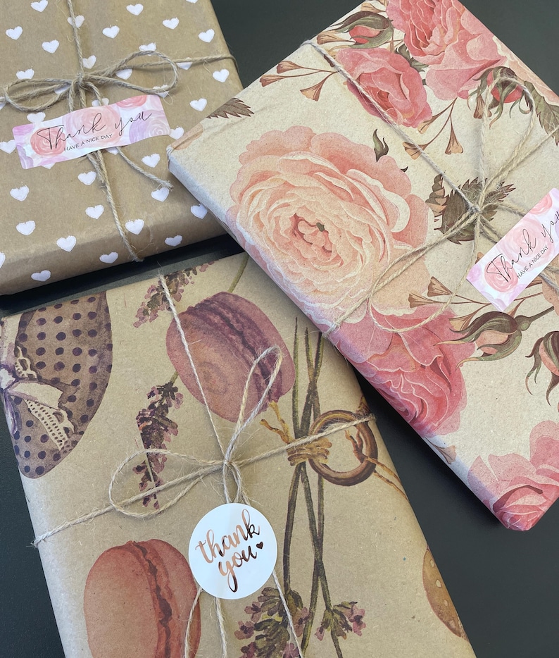 May include: Wrapped gifts with decorative paper and twine. One gift is wrapped in brown paper with white hearts, another with pink roses, and a third with macarons and lavender. Each gift has a "Thank you" sticker.