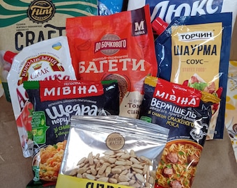 Può includere: Assortimento di prodotti alimentari confezionati, tra cui patatine, salse e pasta. Le confezioni presentano vari colori e testo in lingua straniera. È visibile anche un sacchetto trasparente di semi di girasole.