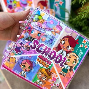 Puede incluir: Un cuaderno con espiral con una cubierta de plástico transparente que presenta ilustraciones de dibujos animados coloridos y el texto "SCHOOL AVATAR WORLD". El cuaderno tiene un borde rosa y varios personajes de dibujos animados.