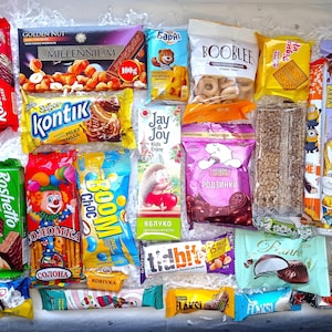 Può includere: Una collezione di varie caramelle e cioccolatini confezionati, tra cui barrette, wafer e biscotti. L'assortimento presenta confezioni colorate con testo e illustrazioni, come un clown, un orso e un coniglio. L'immagine mostra una varietà di dolcetti.