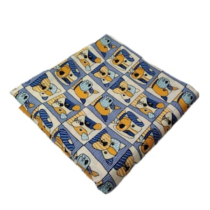 Puede incluir: Una tela blanca con un patrón azul y amarillo de perros de dibujos animados que llevan sombreros. Los perros están en cuadrados con bordes rayados azules y blancos.