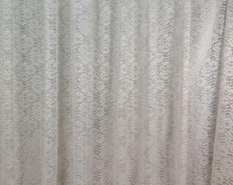 May include: A white lace curtain with a floral design. The curtain is made of a delicate, sheer material and hangs in soft folds. The bottom edge has a scalloped trim. The overall effect is elegant and airy.