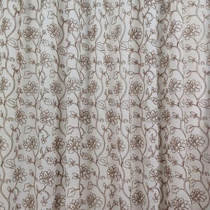 Può includere: Pannello di tenda bianco sporco con un motivo floreale ripetuto in ricamo marrone. Il design presenta fiori e viti stilizzati, creando un'estetica delicata ed elegante. Il tessuto sembra leggero e semitrasparente.