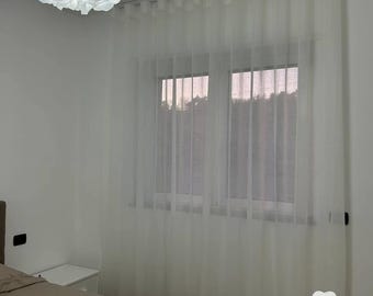 May include: White sheer curtains with a white ceiling track system in a bedroom with a bed and a white nightstand. The curtains are drawn and the room is well-lit. The text "Tende Arredo Tessile" is visible in the lower right corner of the image.