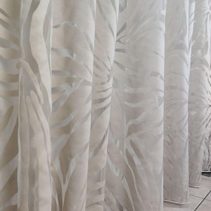 May include: Pale cream-coloured curtains with a delicate zebra stripe design. The fabric is translucent, allowing light to pass through. The curtains hang in vertical folds, creating a flowing, elegant appearance. The design is neutral and suitable for various interior styles.