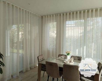 May include: Sheer white curtains hang in a room with a dining table and chairs. The curtains are floor-to-ceiling and frame the windows. The dining table is rectangular with a glass top and is surrounded by six upholstered chairs.
