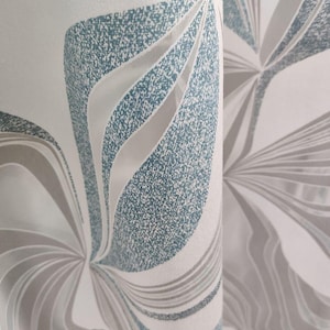 May include: Close-up of a white curtain with a repeating abstract pattern. The design features flowing shapes in shades of grey and teal, creating a textured, layered effect. The fabric is folded, showing the pattern's continuity.