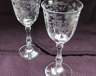 May include: Two clear glass wine glasses with etched floral designs. The glasses have a tall, slender stem and a round bowl.