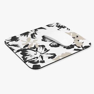 May include: A rectangular mousepad with a floral pattern in black and tan against a white background. A white wireless mouse rests on the mousepad. The mousepad has a black border.