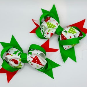 May include: Two green and white Christmas tree patterned hair bows with red accents. The bows are tied with white ribbon and have green and red accents.