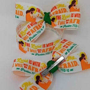 May include: A white ribbon with a green bow and a silver clip. The ribbon has a picture of Jesus and the text "The Lord is with me, I will not be afraid. Psalm 778:6".