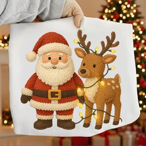 Könnte beinhalten: Eine weiße Weihnachtstasche mit einem Cartoon-Weihnachtsmann und einem Rentier, das mit Lichterketten geschmückt ist. Der Weihnachtsmann trägt einen roten Anzug und Hut, während das Rentier braun mit Geweih ist. Im Hintergrund ist ein Weihnachtsbaum zu sehen.