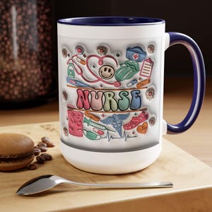 Puede incluir: Taza de cerámica blanca con interior y asa azules. La taza presenta un diseño colorido con la palabra "NURSE" e ilustraciones de temática médica, incluyendo un estetoscopio, un corazón y una carita sonriente. La taza está sobre una superficie de madera.