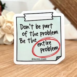 Puede incluir: Pegatina blanca con fondo azul y texto negro que dice "No seas parte del problema Sé todo el problema" con la palabra "todo" encerrada en rojo. La pegatina tiene un borde blanco y una pequeña pestaña negra en la parte superior. El texto "@meimeimade" está en la parte inferior de la pegatina.