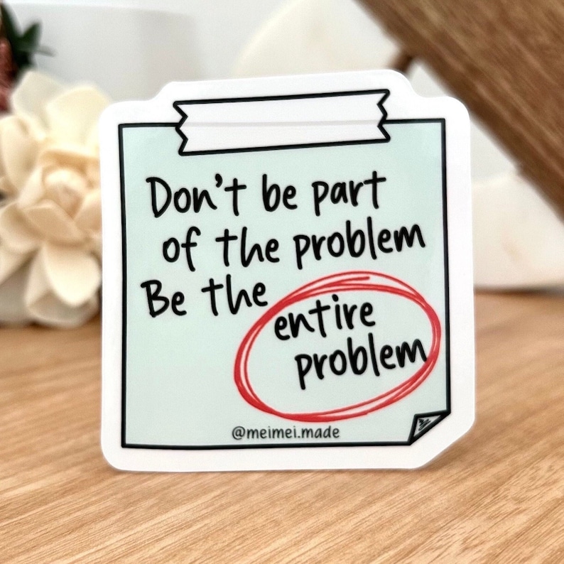 May include: White sticker with a blue background and black text that reads "Don't be part of the problem Be the entire problem" with the word "entire" circled in red. The sticker has a white border and a small black tab at the top. The text "@meimeimade" is at the bottom of the sticker.