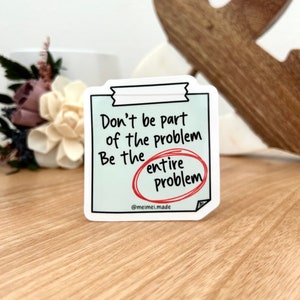 May include: A white sticker with a blue background and black text that reads "Don't be part of the problem. Be the entire problem." The word "entire" is circled in red.