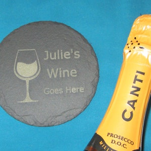 Puede incluir: Un posavasos de pizarra negra con el texto "Julie's Wine Goes Here" y un gráfico de copa de vino. Una botella de Canti Prosecco D.O.C. está en el fondo.