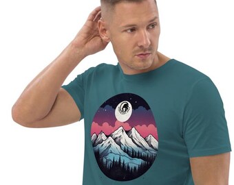 May include: A teal blue t-shirt with a graphic of a mountain range with a full moon and stars in the sky. The mountains are white with pink and blue hues in the sky.