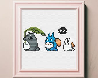Puede incluir: Una bordado de punto de cruz con tres personajes de la película animada Mi vecino Totoro. Los personajes son Totoro, una criatura grande, peluda y gris con orejas grandes, un Totoro azul más pequeño con una mochila y una criatura blanca similar a un gato con orejas grandes. El fondo es blanco.