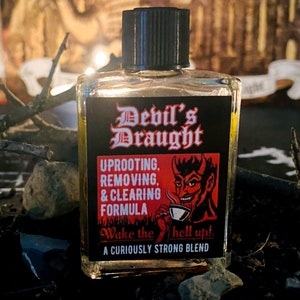 Op de afbeelding: Een kleine, heldere glazen fles met een zwarte dop. Het etiket leest "Devil's Draught" in rode gotische letters, met een rode duivel illustratie. De tekst hieronder luidt "Uprooting, Removing, & Clearing Formula" en "Wake the hell up!"