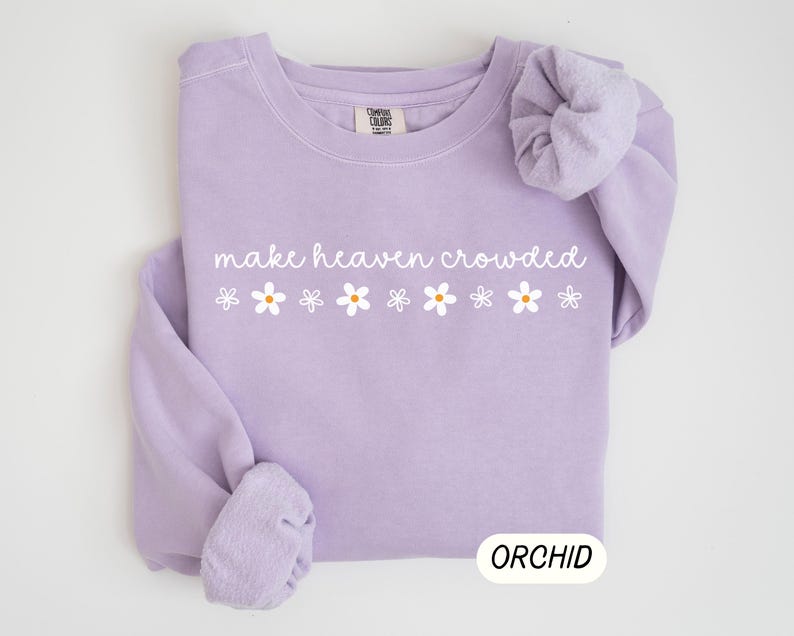 K&ouml;nnte beinhalten: Ein helllila Sweatshirt mit dem wei&szlig;en Schriftzug "make heaven crowded" und sechs wei&szlig;en G&auml;nsebl&uuml;mchen. Das Wort "ORCHID" ist in einem wei&szlig;en Rechteck unten aufgedruckt. Das Sweatshirt ist aus weichem Material.