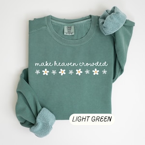 K&ouml;nnte beinhalten: Hellgr&uuml;nes Sweatshirt mit dem wei&szlig;en Schriftzug "make heaven crowded" und wei&szlig;en G&auml;nsebl&uuml;mchen. Die &Auml;rmel sind gefaltet. Unten rechts befindet sich ein Etikett mit der Aufschrift "LIGHT GREEN".
