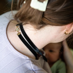 May include: A black velvet choker necklace with a gold-colored star pendant adorned with small, clear rhinestones. The necklace is worn around the neck, and the image shows a close-up of the necklace and the person wearing it.