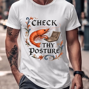 May include: White t-shirt with a graphic design featuring a cartoon shrimp using a laptop. The text reads "CHECK THY POSTURE" in a decorative font, surrounded by floral elements. The shrimp is orange, and the laptop is brown.