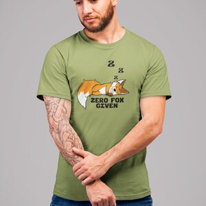 May include: Olive green t-shirt featuring a cartoon fox sleeping with the text "ZERO FOX GIVEN". The fox is orange and white. Two "Z" symbols are above the fox's head. The shirt is worn by a person.
