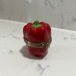 Könnte beinhalten: Eine rote Keramik-Schmuckdose in Form einer Paprika mit einem goldenen Scharnierdeckel. Der Deckel hat ein kleines Bienenmotiv.