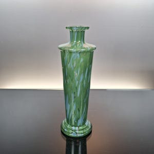 May include: A tall, green glass vase with a flared base and a narrow neck. The vase has a speckled pattern of white and blue throughout the green glass. The vase is approximately 10 inches tall.