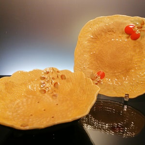 Könnte beinhalten: Zwei gelbe Keramikschalen mit einer strukturierten Oberfläche und einem erhabenen Design aus Blättern und roten Beeren. Die größere Schale ist eine Servierplatte und die kleinere Schale ist eine Obstschale.