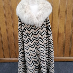 May include: A long, black, white and beige fur coat with a large, white fur collar. The coat has a chevron pattern.