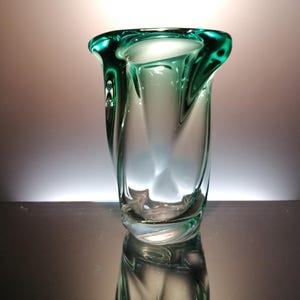 May include: A clear glass vase with a green rim. The vase has a unique, twisted design.