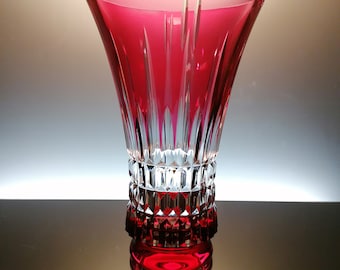 Puede incluir: Un jarrón de cristal rojo con una base de cristal transparente y un diseño de vidrio cortado. El jarrón tiene una boca ancha y una base estrecha.
