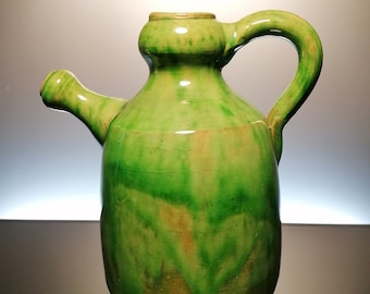 May include: A green ceramic pitcher with a handle and a spout. The pitcher has a mottled green glaze with streaks of brown.