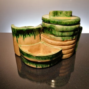 May include: A ceramic multi-tiered dish with green and yellow glaze. The dish has three sections, one round and two oval. The round section has a lid.
