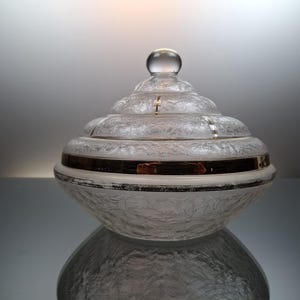 May include: A clear glass lidded dish with a gold band around the rim. The dish has a frosted, textured surface and a rounded, dome-shaped lid.