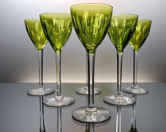 May include: Set of six green glass stemmed wine glasses with a textured design. The glasses are arranged in a semi-circle on a reflective surface.