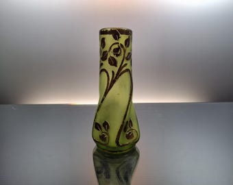 Könnte beinhalten: Eine schlanke, hellgrüne Glasvase mit braunem Blumendesign. Die Vase hat eine leicht geschwungene Form und einen ausgestellten Boden. Der Rand und die floralen Details sind braun. Die Vase dient wahrscheinlich dekorativen Zwecken.