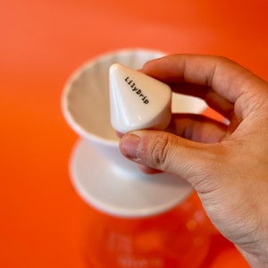 K&ouml;nnte beinhalten: Ein wei&szlig;er Kaffeefilter aus Keramik mit einem kegelf&ouml;rmigen Filter, der mit "Lilydrip" beschriftet ist.