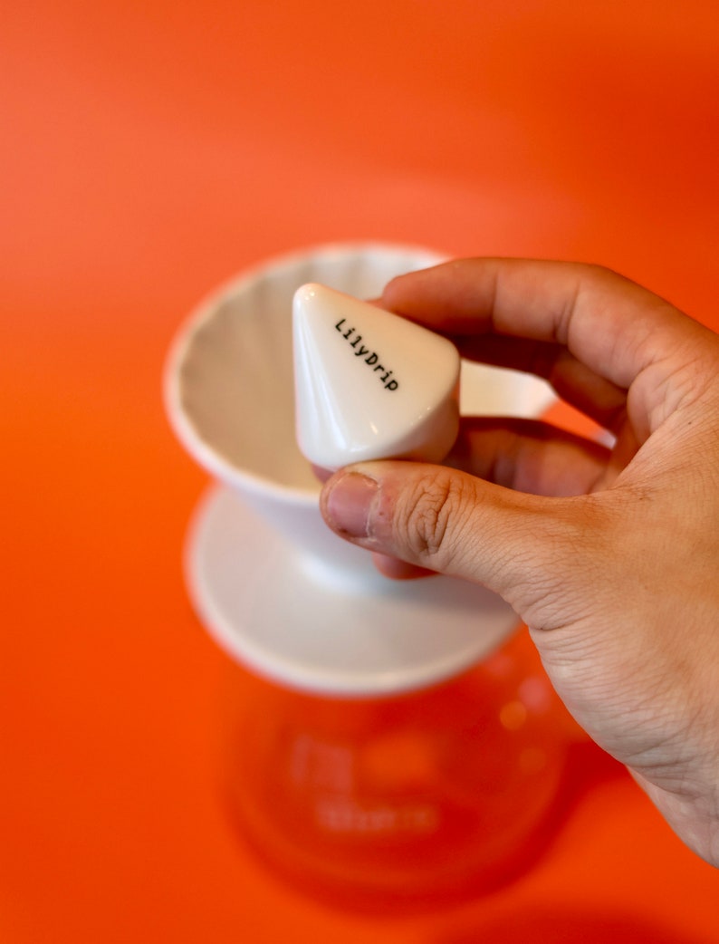 K&ouml;nnte beinhalten: Ein wei&szlig;er Kaffeefilter aus Keramik mit einem kegelf&ouml;rmigen Filter, der mit "Lilydrip" beschriftet ist.